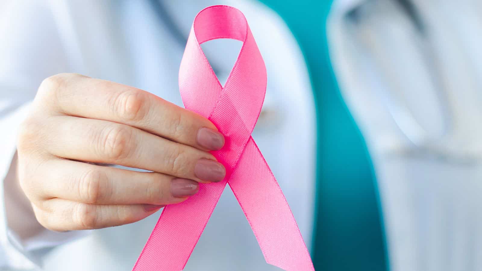 Pink ribbon for breast cancer awareness held by a healthcare professional.