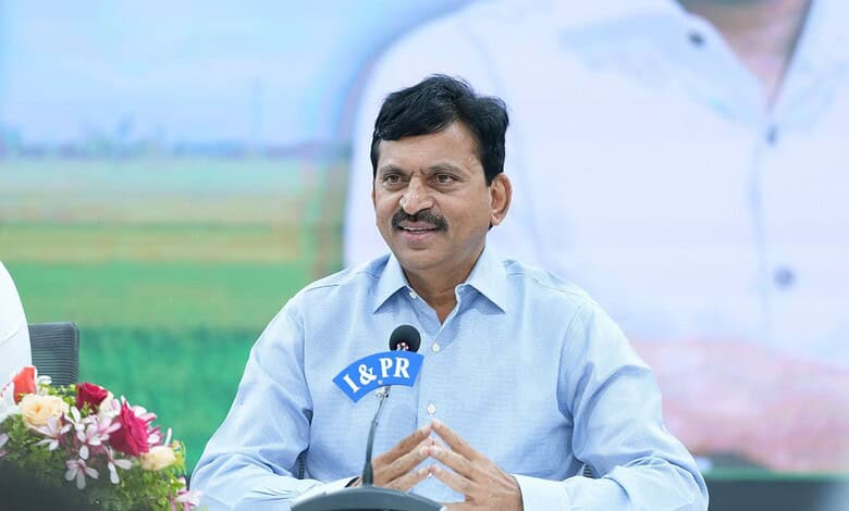 A man in a light blue shirt speaking at a press conference outdoors with a microphone labeled "I & PR".