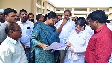 The Siasat Daily, officials reviewing documents with a woman in a blue saree during an outdoor event.