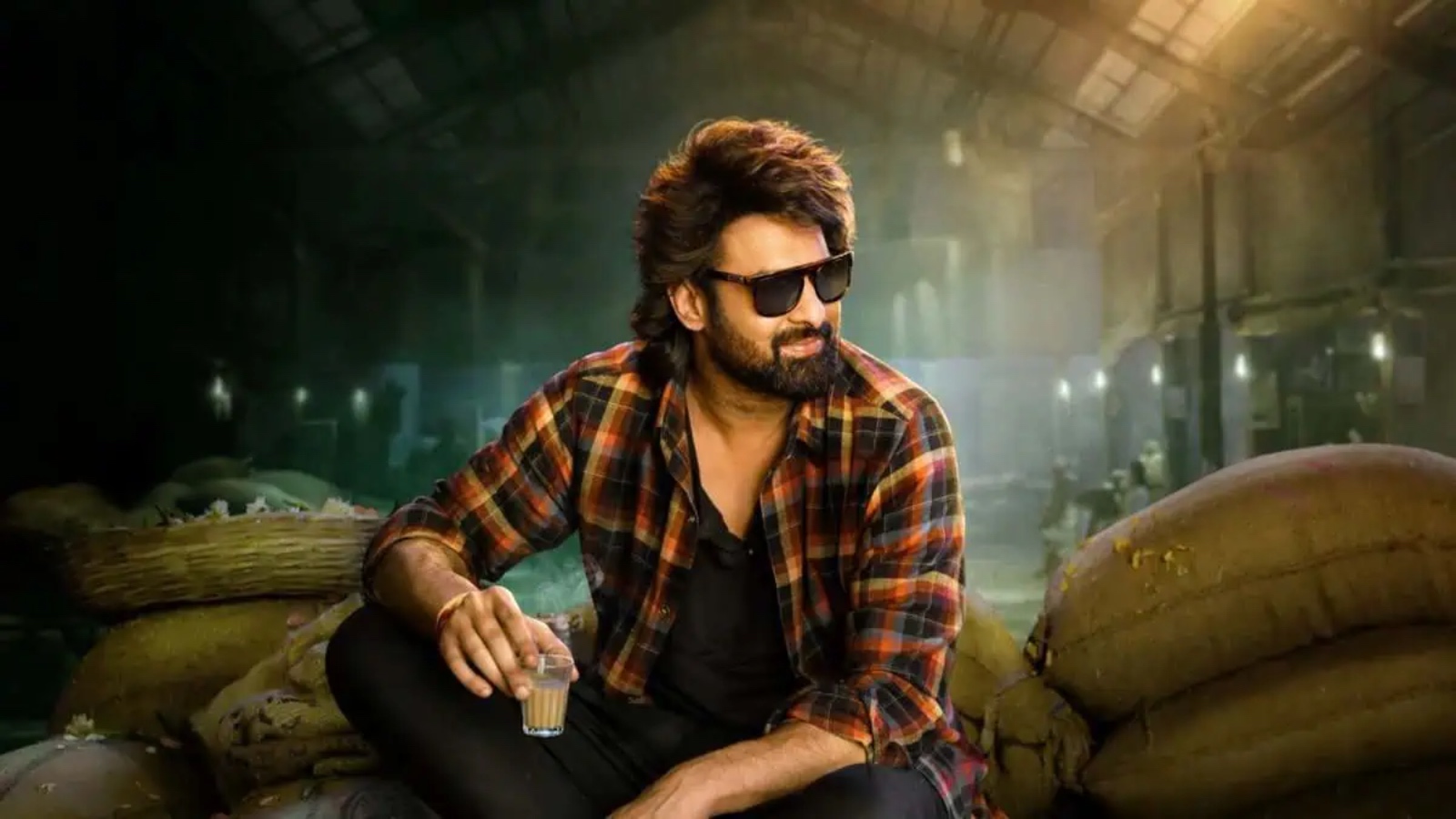 Stylish man in sunglasses relaxing in an industrial warehouse with sacks and warm lighting.