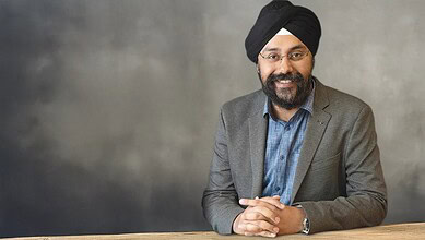 Prabhjeet Singh smiling in a grey blazer and blue shirt against a grey background.
