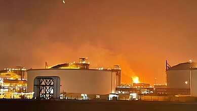 Fire and smoke rise from a gas plant at night, with industrial tanks in the foreground.