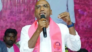 Prominent man speaking passionately at a public event, wearing a white shirt and pink scarf, with a pink.