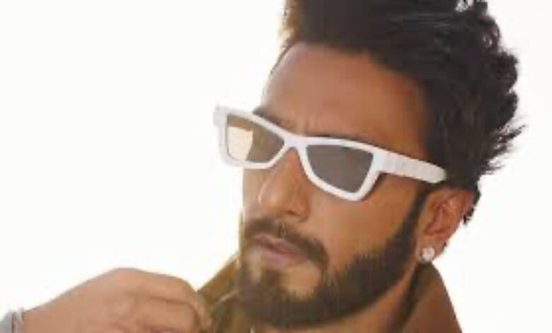 A young man with dark hair and beard wearing white sunglasses and a yellow shirt, looking thoughtfully to.