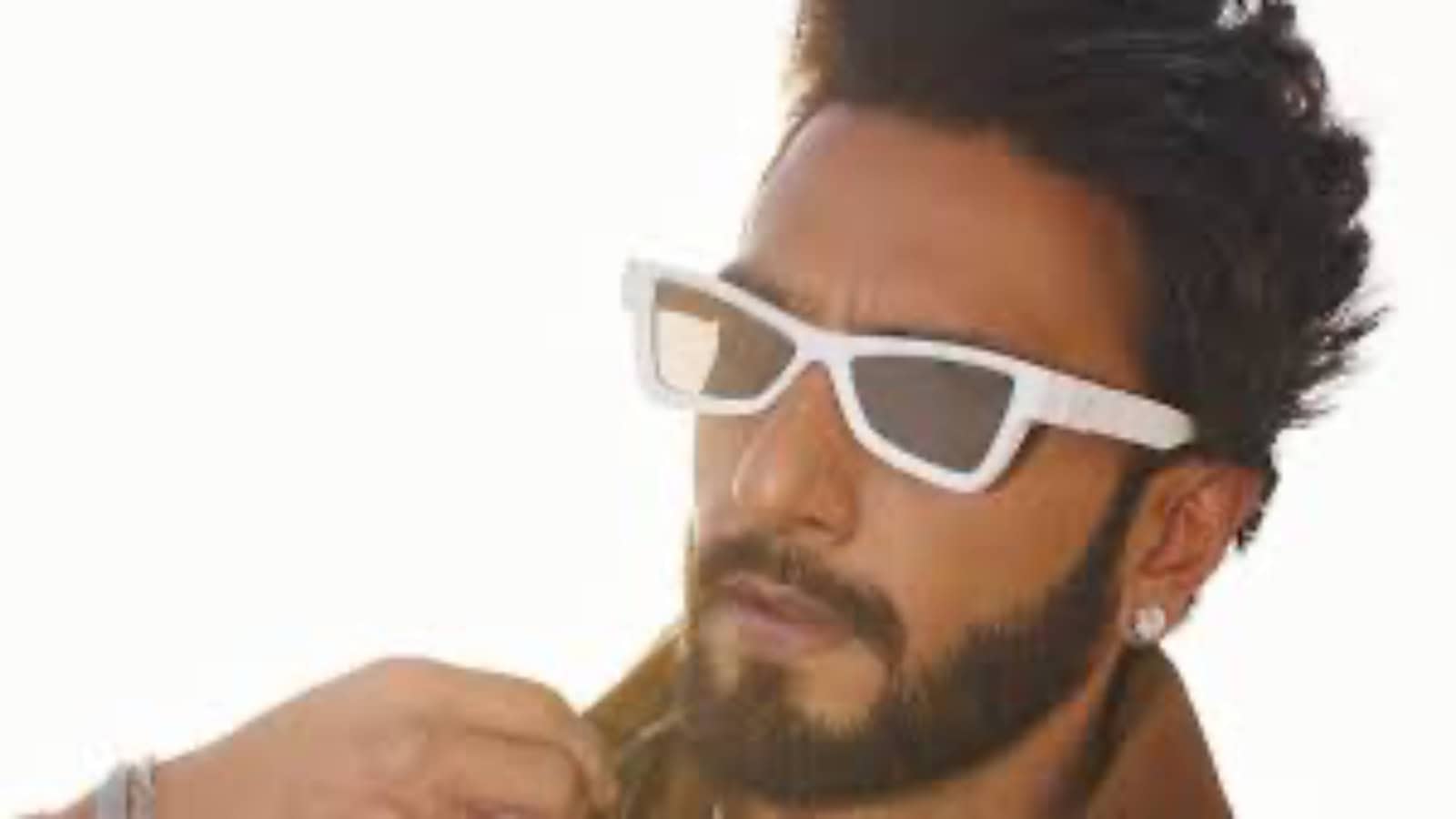 A young man with dark hair and beard wearing white sunglasses and a yellow shirt, looking thoughtfully to.