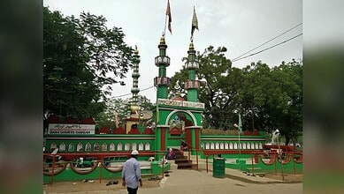 Vishweshwaraya Swamy Temple with vibrant green and red architecture, surrounded by lush trees and cloudy.
