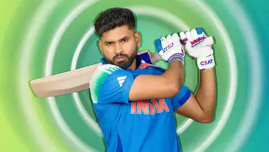 Cricketer holding a bat and wearing gloves, ready to play cricket, against a vibrant green background.