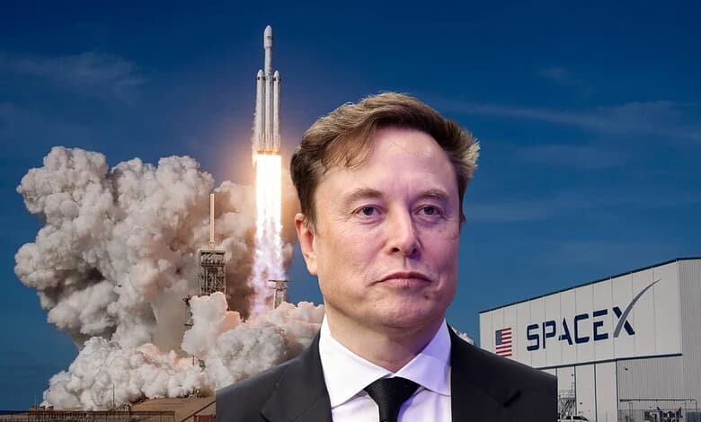 SpaceX rocket launch with Elon Musk in front, clear blue sky, and SpaceX building in background.