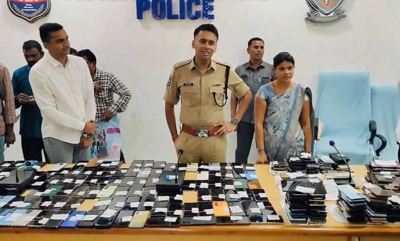 A police officer and officials displaying seized mobile phones and electronic devices at a press conferen.