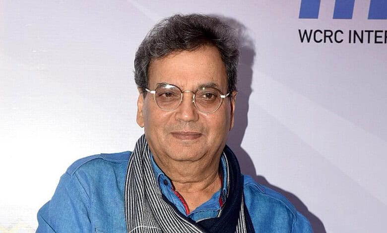 A middle-aged Indian man with glasses, wearing a blue shirt and scarf, attending a formal event with a ba.