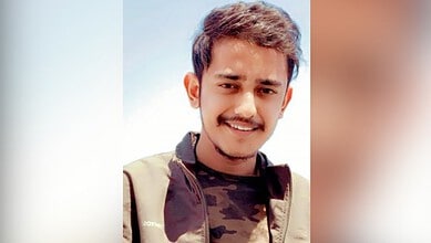 Young man with a smile, wearing a camouflage jacket, outdoors on a sunny day.