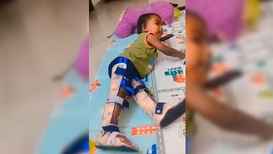 A child lying on a colourful play mat with toys and a purple pillow, engaging in imaginative play or rest.