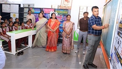Teacher explains chalk swapping activity to students and officials in Telangana school classroom.