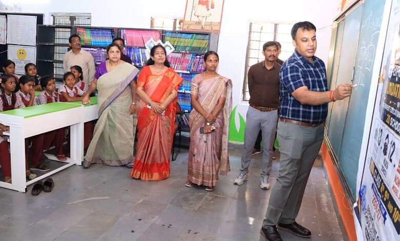 Teacher explains chalk swapping activity to students and officials in Telangana school classroom.