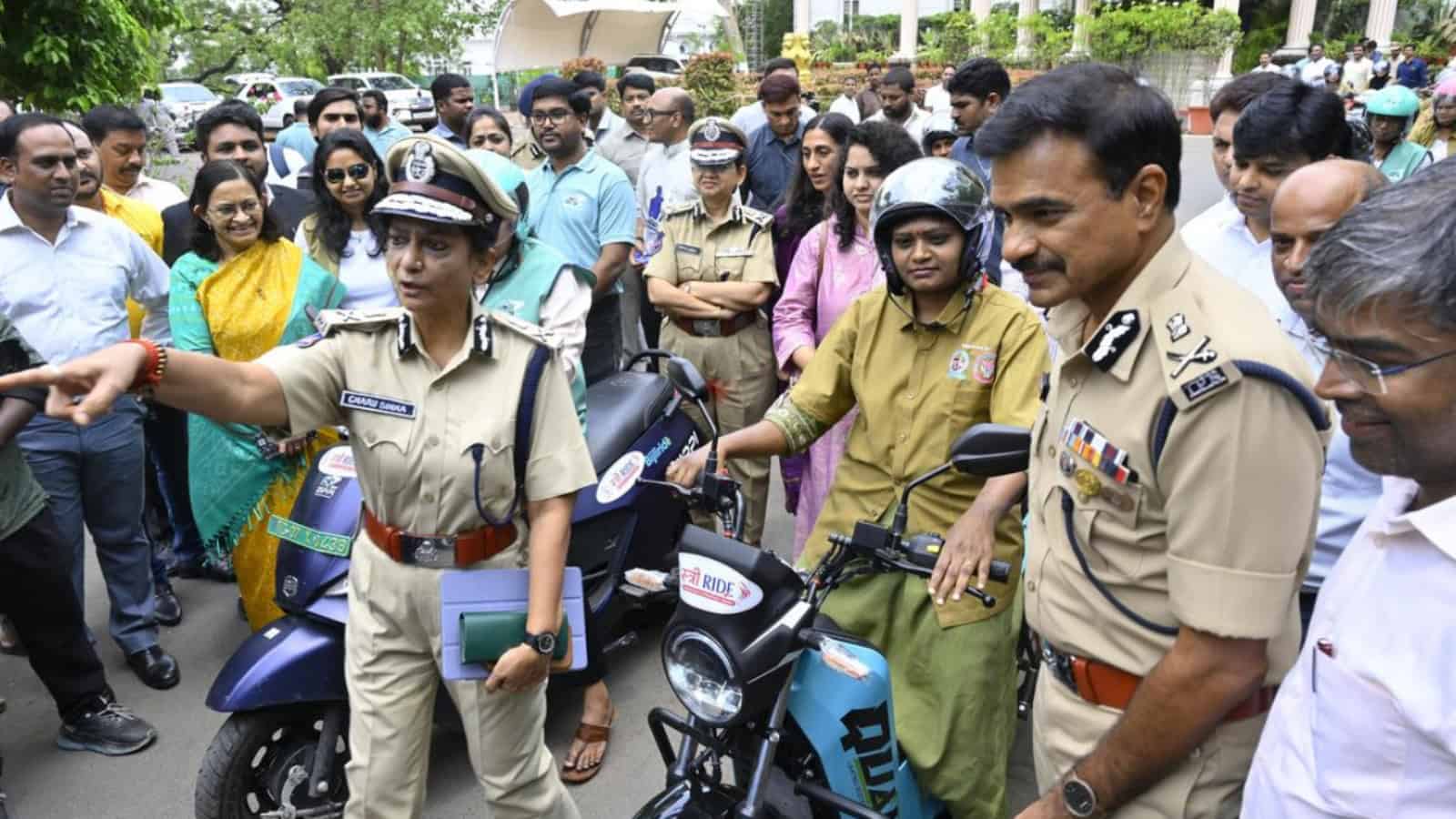 Police officers engaging with a crowd during a public event in India, with onlookers and motorcycles pres.