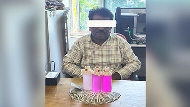 A man sitting at a desk with three pink bottles and a decorative tray in front of him.
