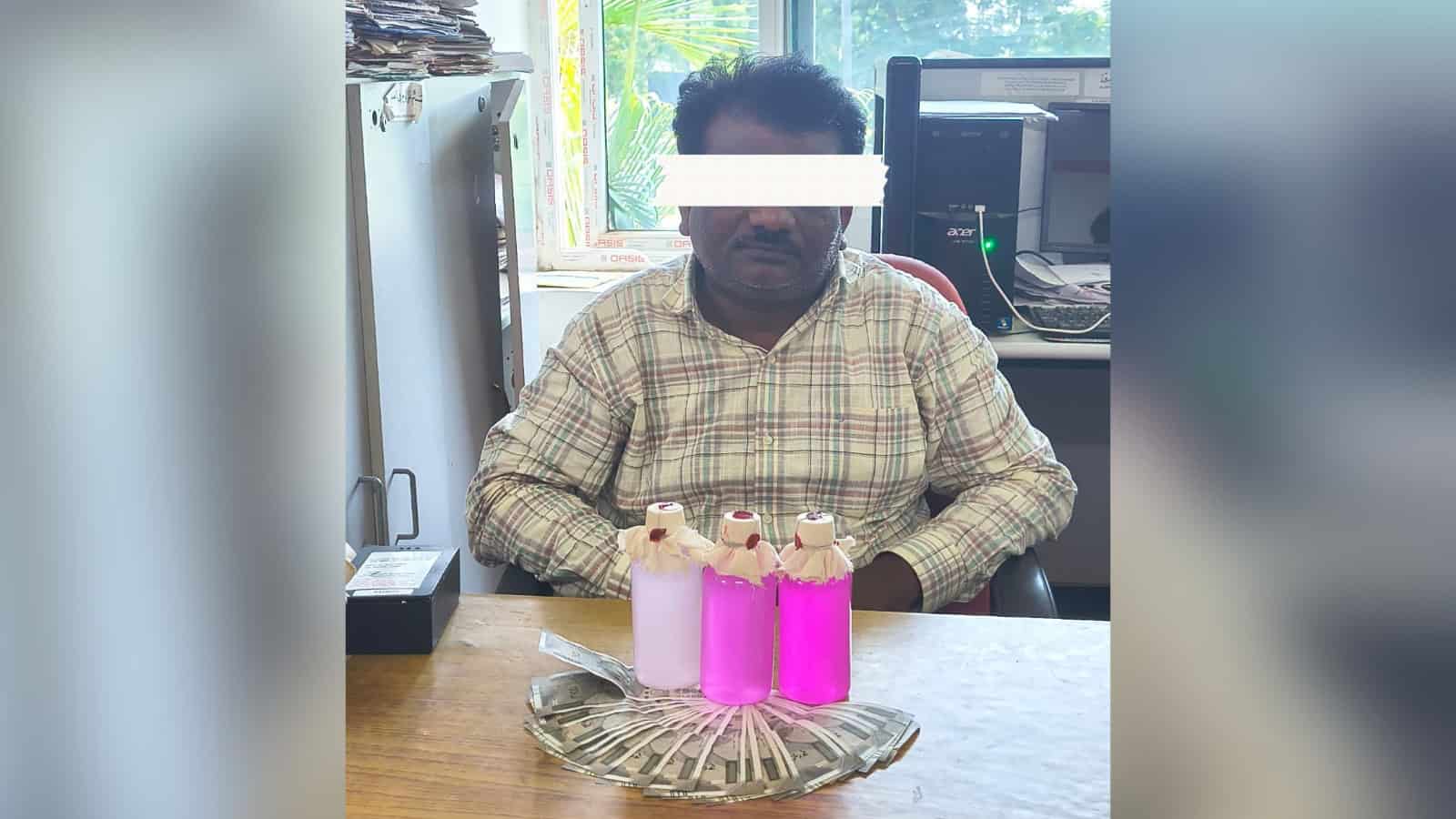 A man sitting at a desk with three pink bottles and a decorative tray in front of him.