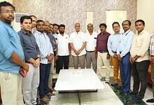 A diverse group of men gathered around a table in an office setting, posing for a group photo.