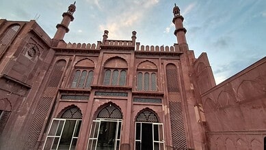 Majestic red sandstone mosque with intricate architecture and tall minarets under a partly cloudy sky.