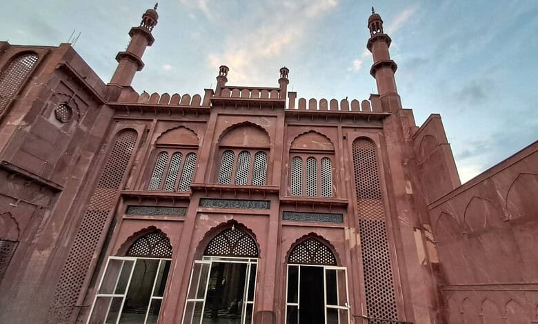 Majestic red sandstone mosque with intricate architecture and tall minarets under a partly cloudy sky.