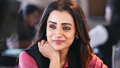 A woman with dark hair and a pink blazer smiling thoughtfully at a professional event, representing confi.