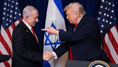 US and Israeli leaders shaking hands during diplomatic meeting with flags in background.