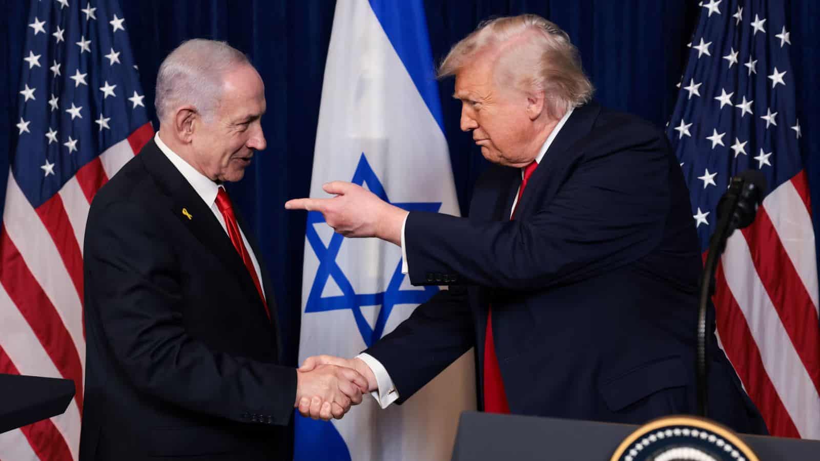 US and Israeli leaders shaking hands during diplomatic meeting with flags in background.