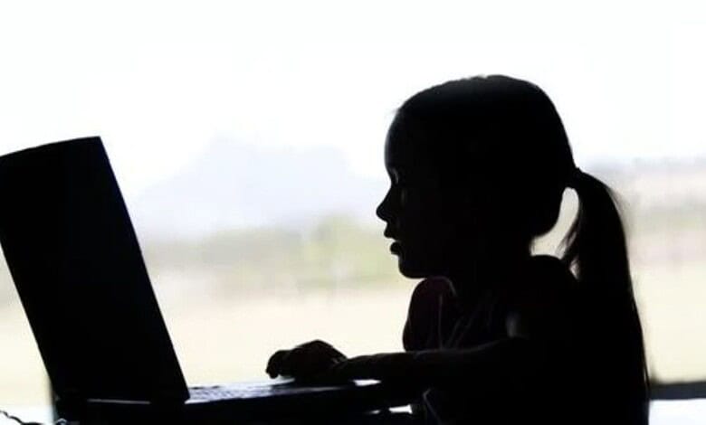 A woman using a laptop, silhouetted against a bright window, working or studying indoors.
