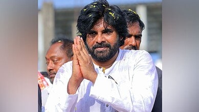 A man with black hair and beard, wearing a white kurta, praying with hands folded outdoors, with other pe.