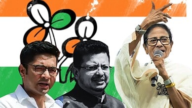 A woman speaking into a microphone with two men standing beside her, set against an Indian flag backgroun.