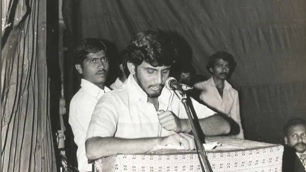 A young man speaking at a microphone during a public event or gathering.