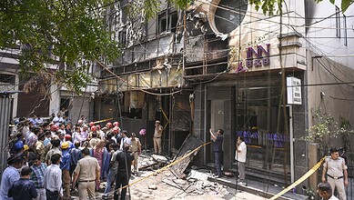 A fire-damaged building with a crowd of people and emergency responders outside, showing the aftermath of.