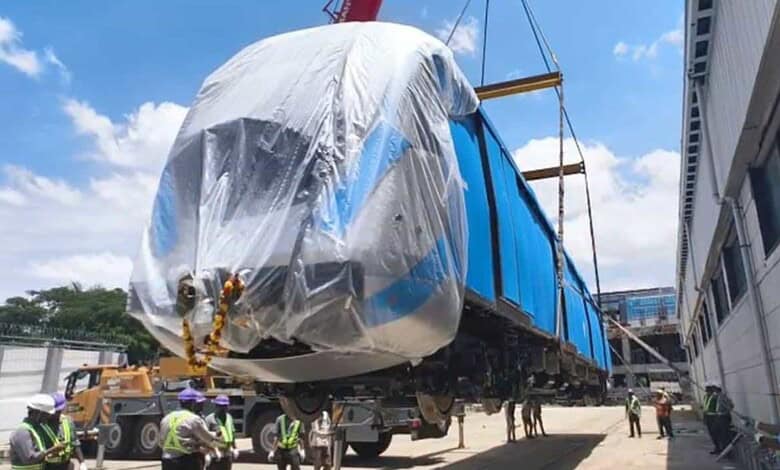 Large blue train carriage covered with plastic wrap being transported on a flatbed truck.