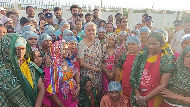 A woman addressing a large gathering of women, many wearing colourful traditional attire and head coverin.