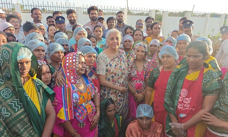 A woman addressing a large gathering of women, many wearing colourful traditional attire and head coverin.