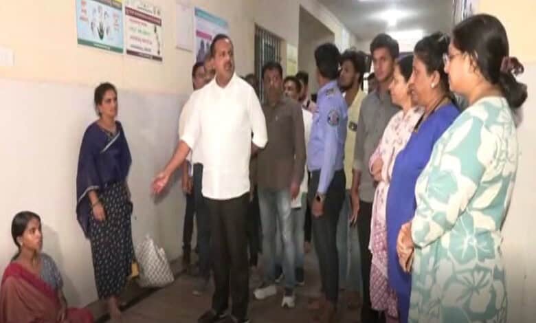 A woman sitting on the floor listening to a man speaking to a group of people in a corridor.