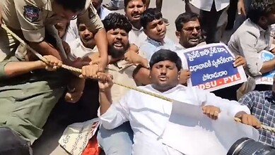 A man in white being pulled into a crowd during a protest or demonstration, with police officers and supp.