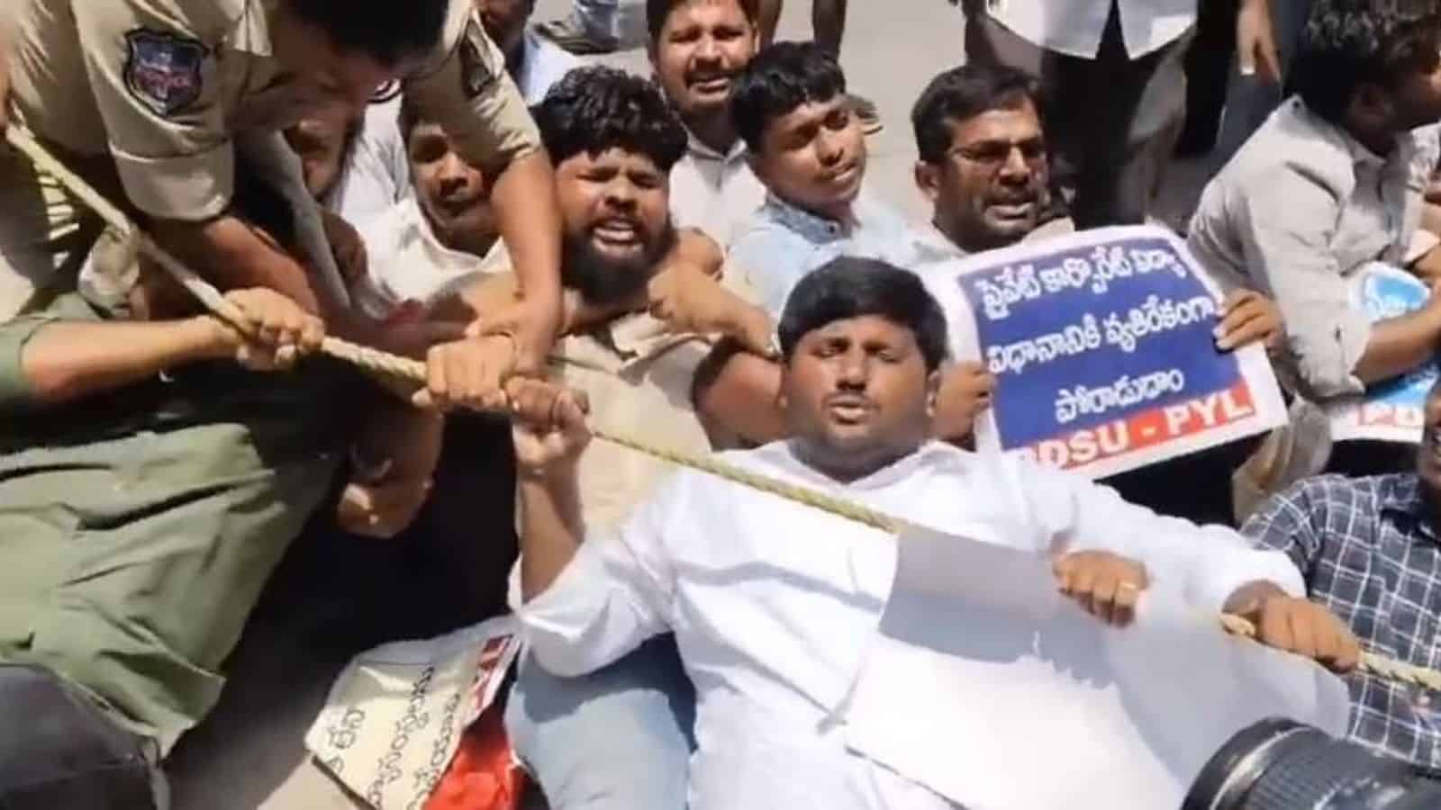 A man in white being pulled into a crowd during a protest or demonstration, with police officers and supp.