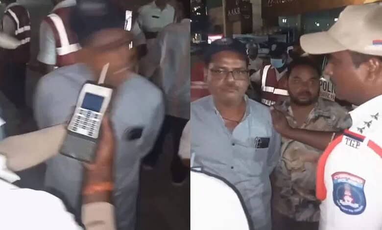 A man being detained by police officers at night, with officers holding a mobile device and engaging with.
