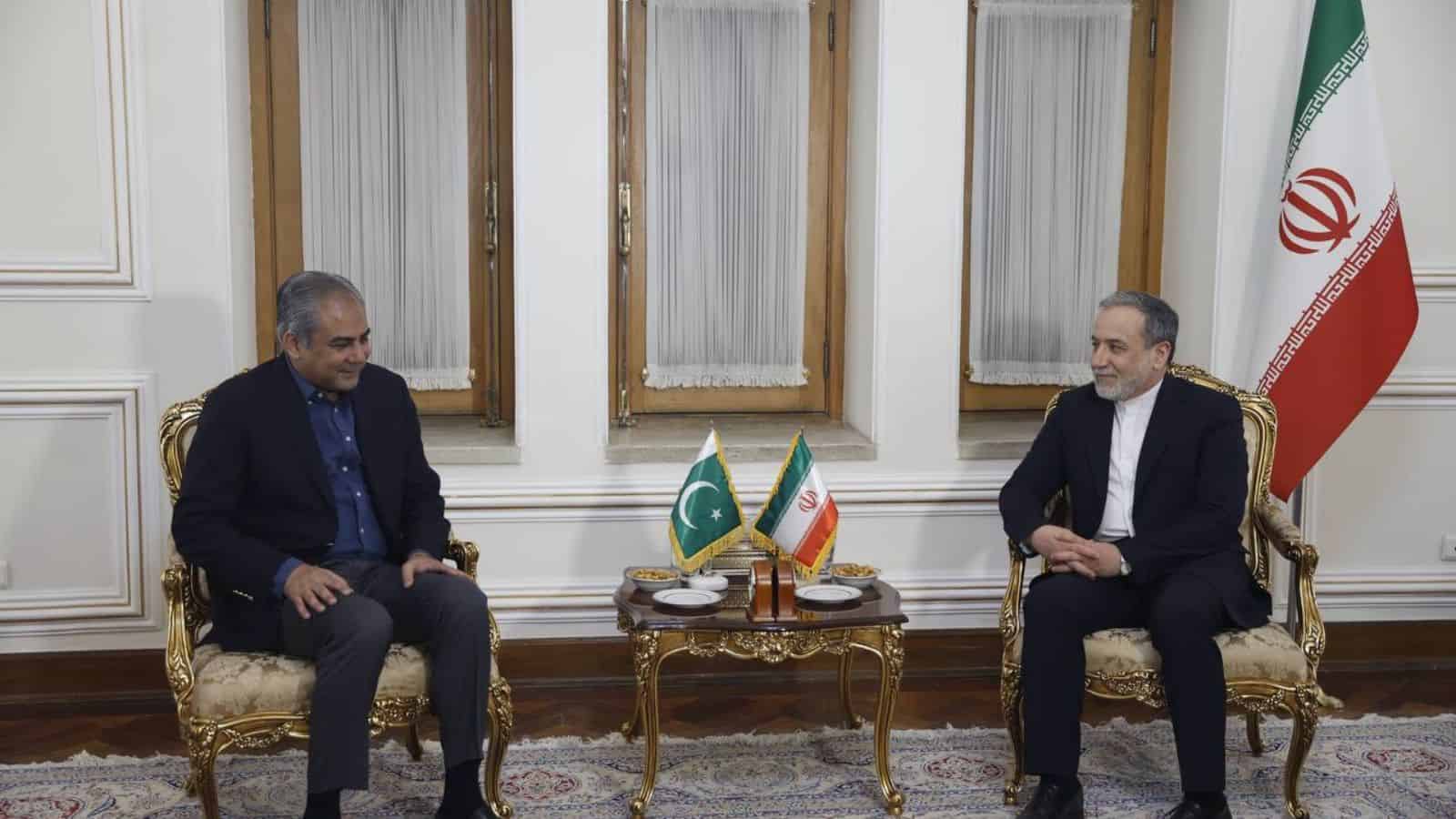 Diplomatic meeting between officials from Pakistan and Iran in an elegant room with national flags, discu.