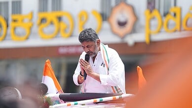 A man in white traditional attire praying with folded hands in front of a microphone during a public even.