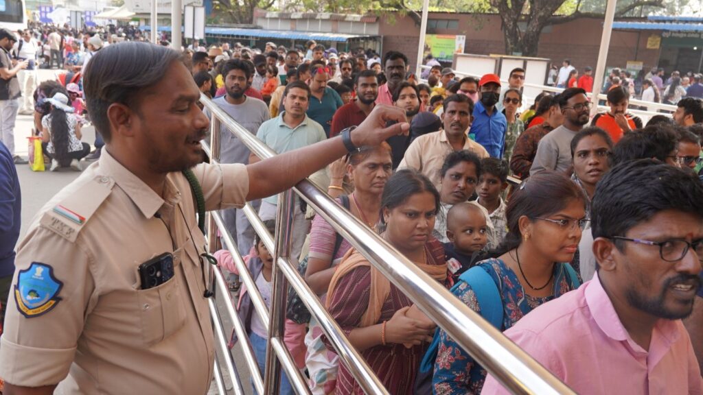 A woman police officer addressing a large crowd at an outdoor event in India.