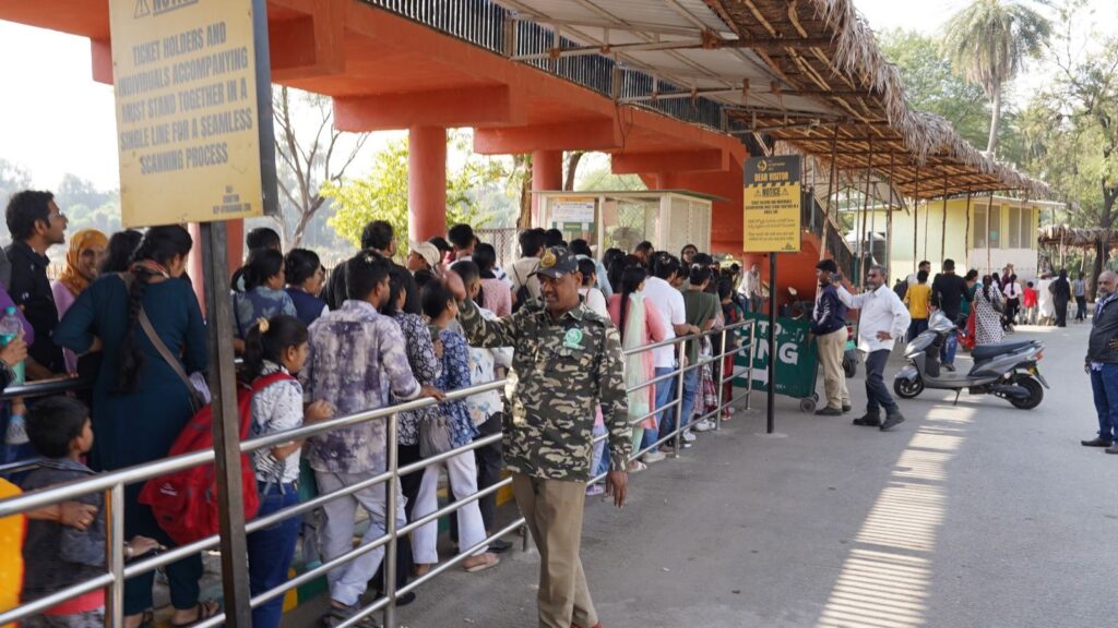 Crowd of people waiting in line at a busy outdoor transportation hub in India.