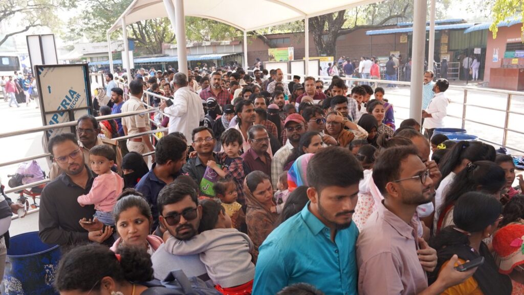 Crowd of people waiting under a tent at an outdoor event in India, with children and adults engaging in v.
