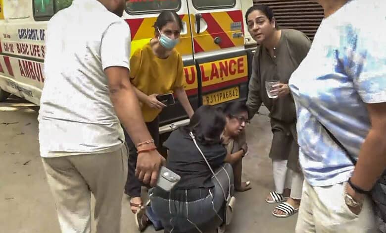 A woman receiving medical assistance from paramedics beside an ambulance on a busy street.