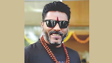 A man wearing sunglasses and traditional attire, smiling at an outdoor event.