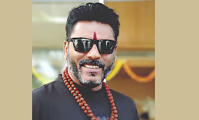 A man wearing sunglasses and traditional attire, smiling at an outdoor event.