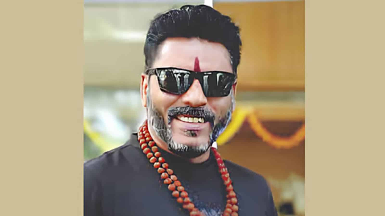 A man wearing sunglasses and traditional attire, smiling at an outdoor event.