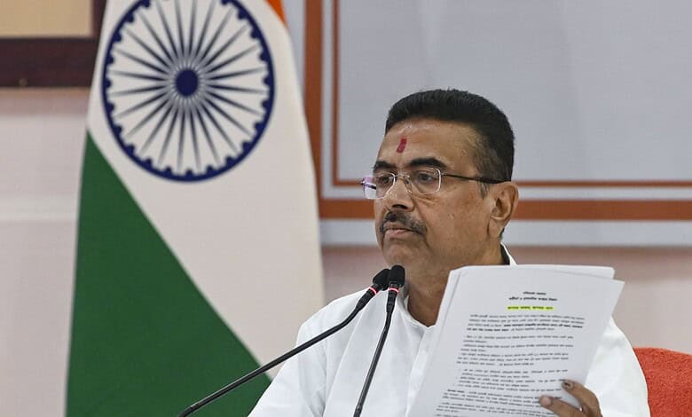 Indian politician speaking at a podium with the Indian flag in the background, wearing glasses and tradit.