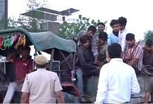 A man selling fruits from a cart with a group of young people gathered around, outdoors in an urban setti.